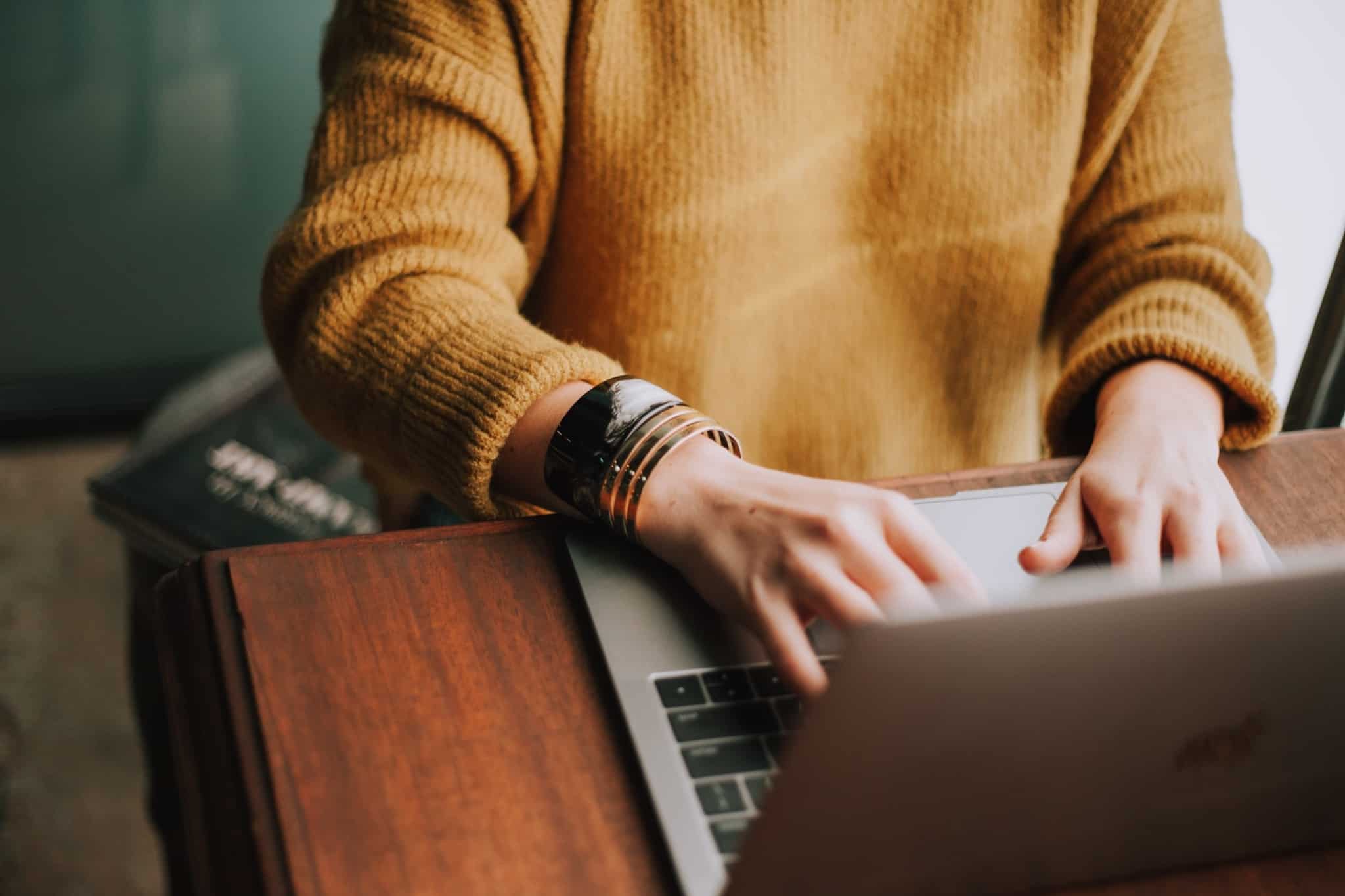 A woman sitting and typing on a laptop on a brown table